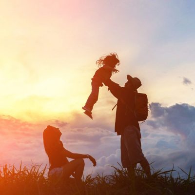 The happy family of three people, mother, father and child in front of a sunset sky.